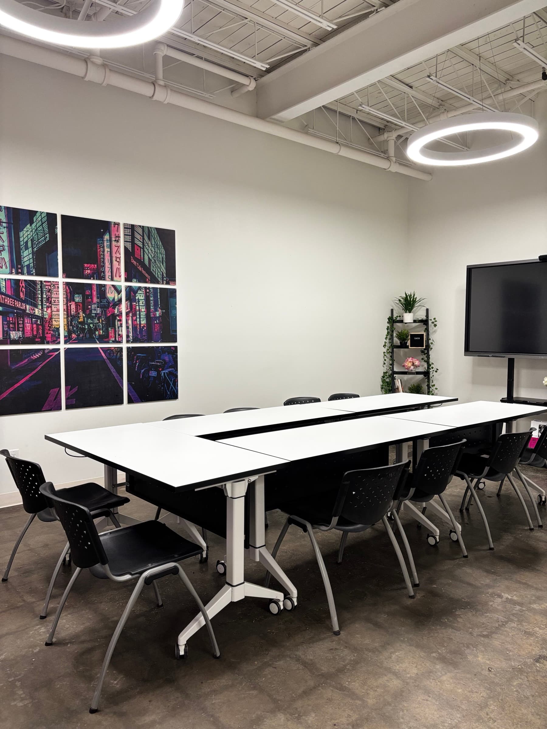 Boardroom with white tables, black chairs, a city-lights art wall and a wall screen at House of Snob in Edmonton