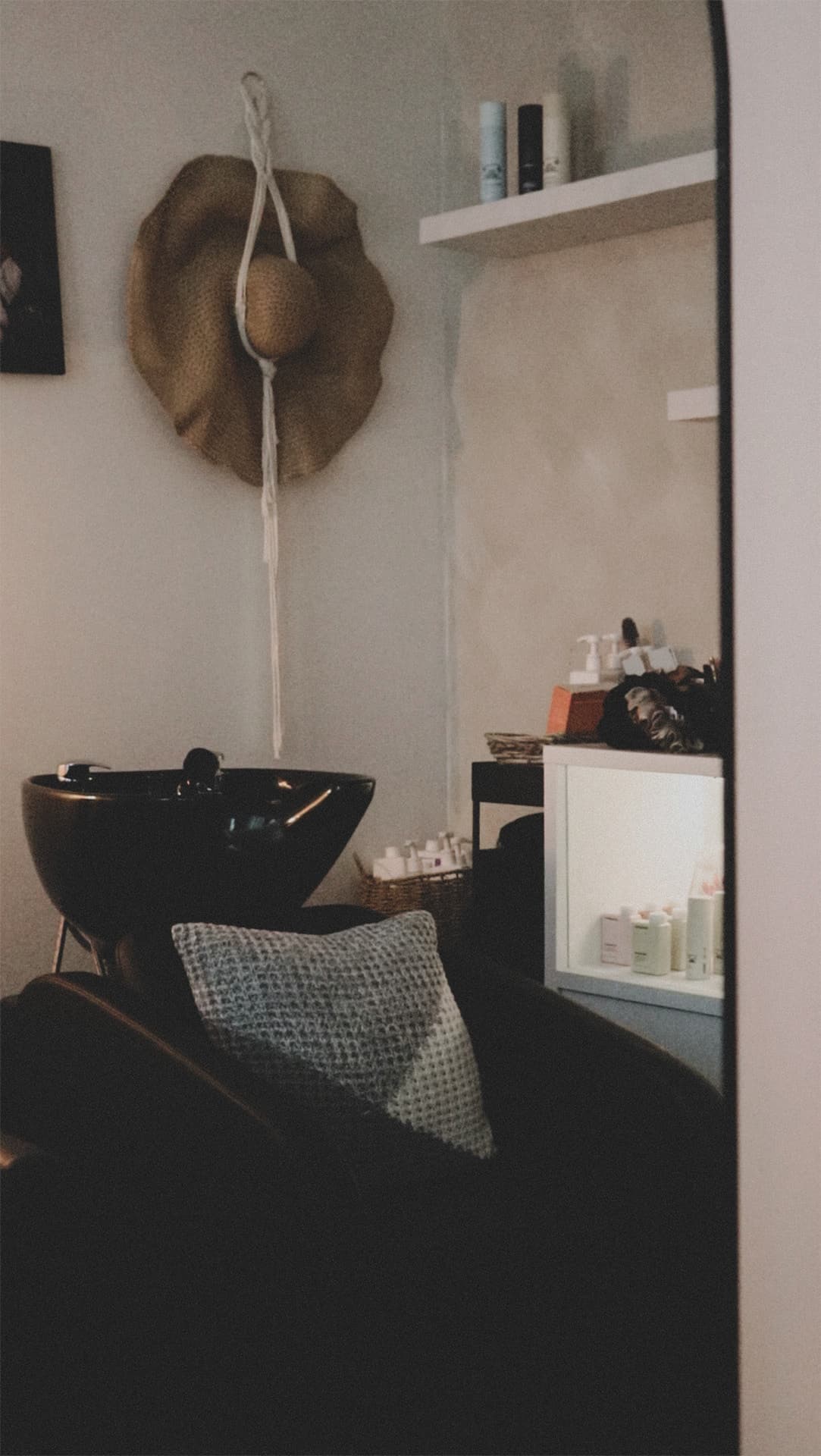 The wash basin and a black shampoo chair with a woven cushion in The Sanctuary, a straw hat hung on the wall above