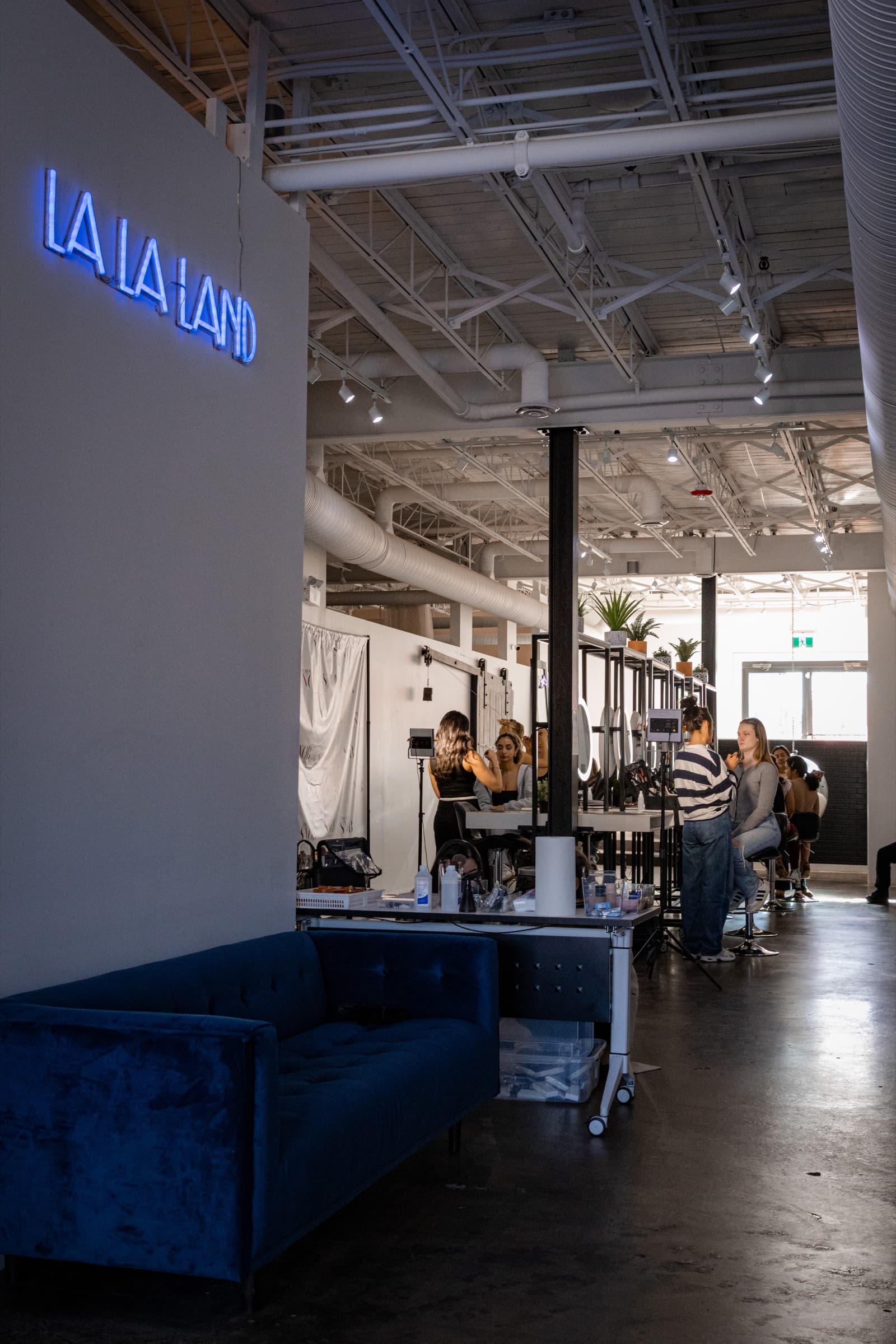 Blue "La La Land" neon sign above a velvet sofa, with artists working at their stations behind, at House of Snob in Edmonton