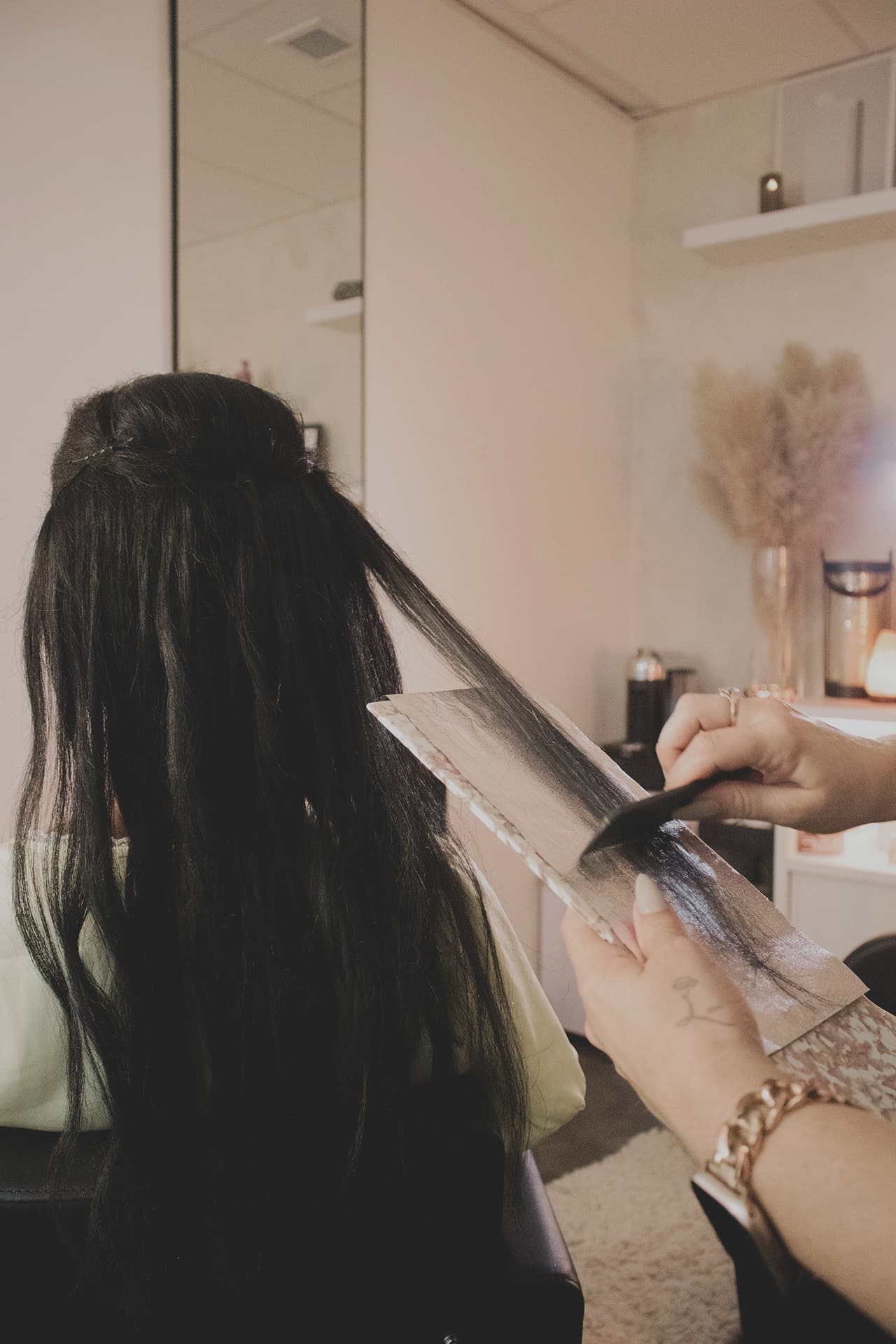A section of long dark hair laid over a foil board as colour is painted through it