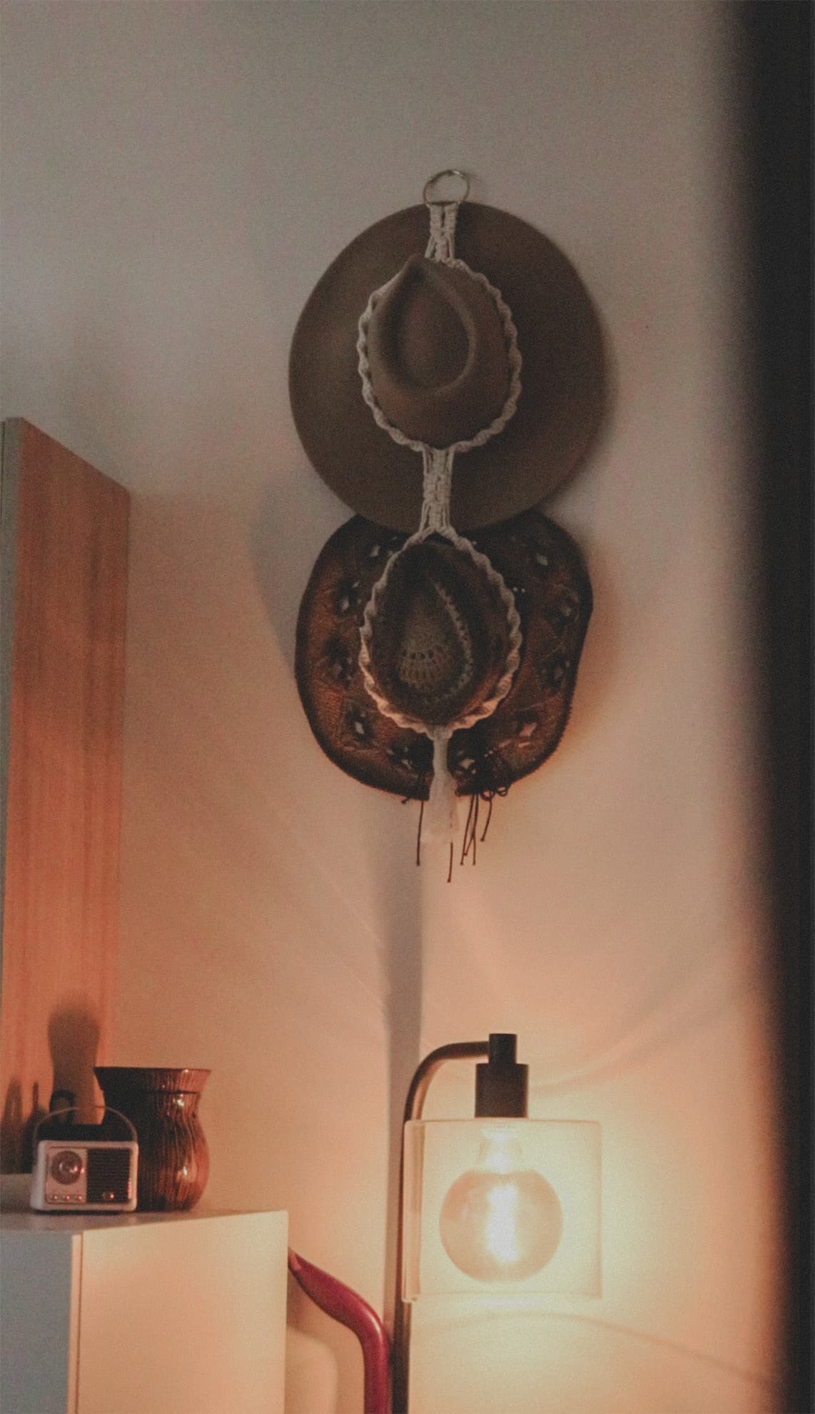 Two hats hung on macramé above a warm glowing lamp in a corner of The Sanctuary