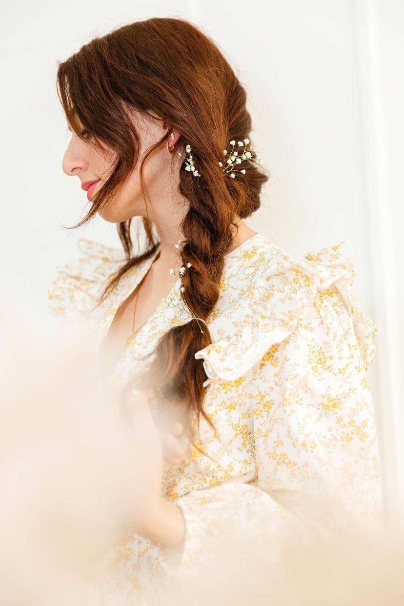 A bride in profile with a loose auburn braid threaded with baby's breath, in a floral ruffled dress