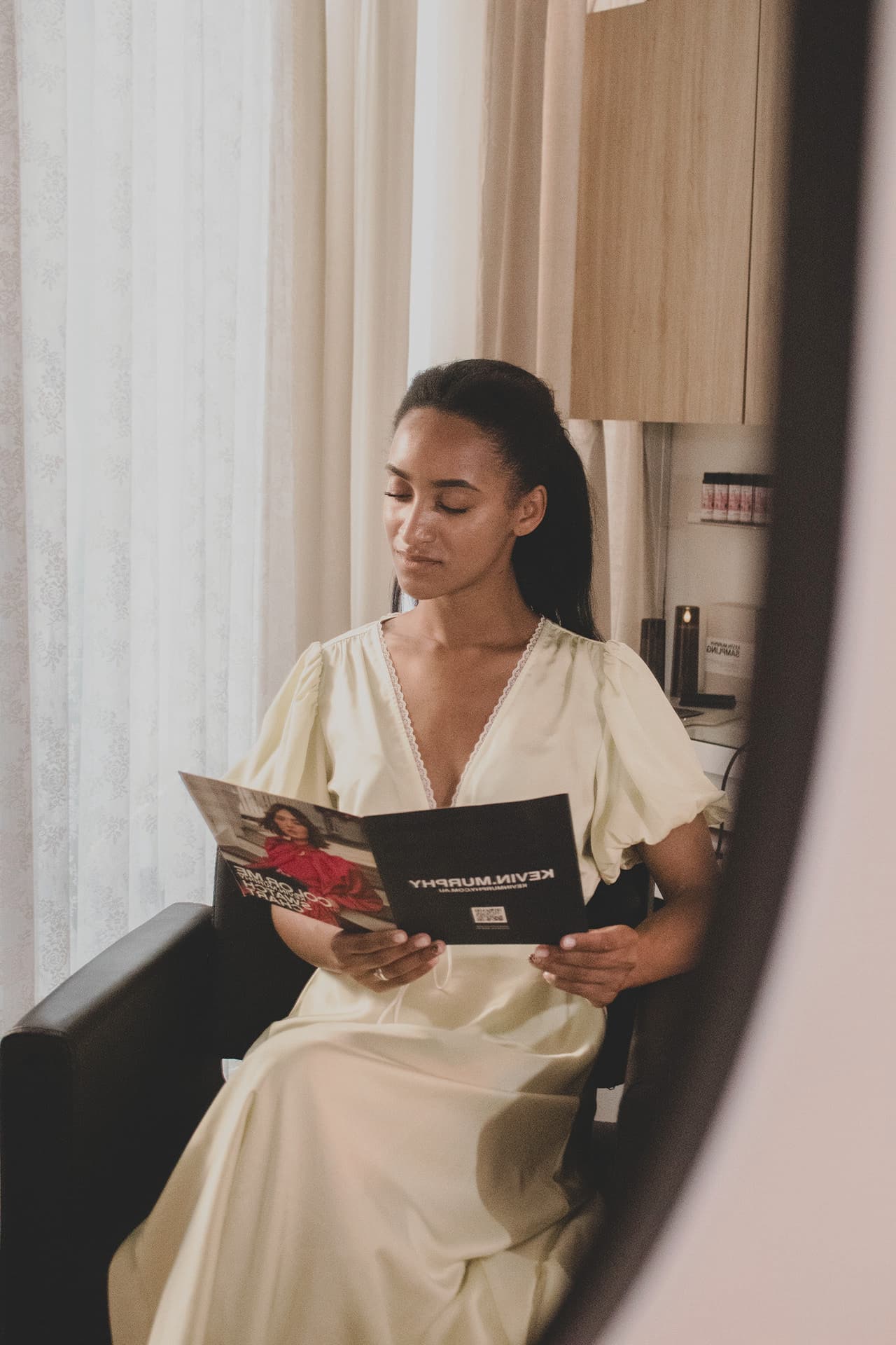 A guest in a cream dress reading a Kevin.Murphy booklet in the styling chair at The Sanctuary