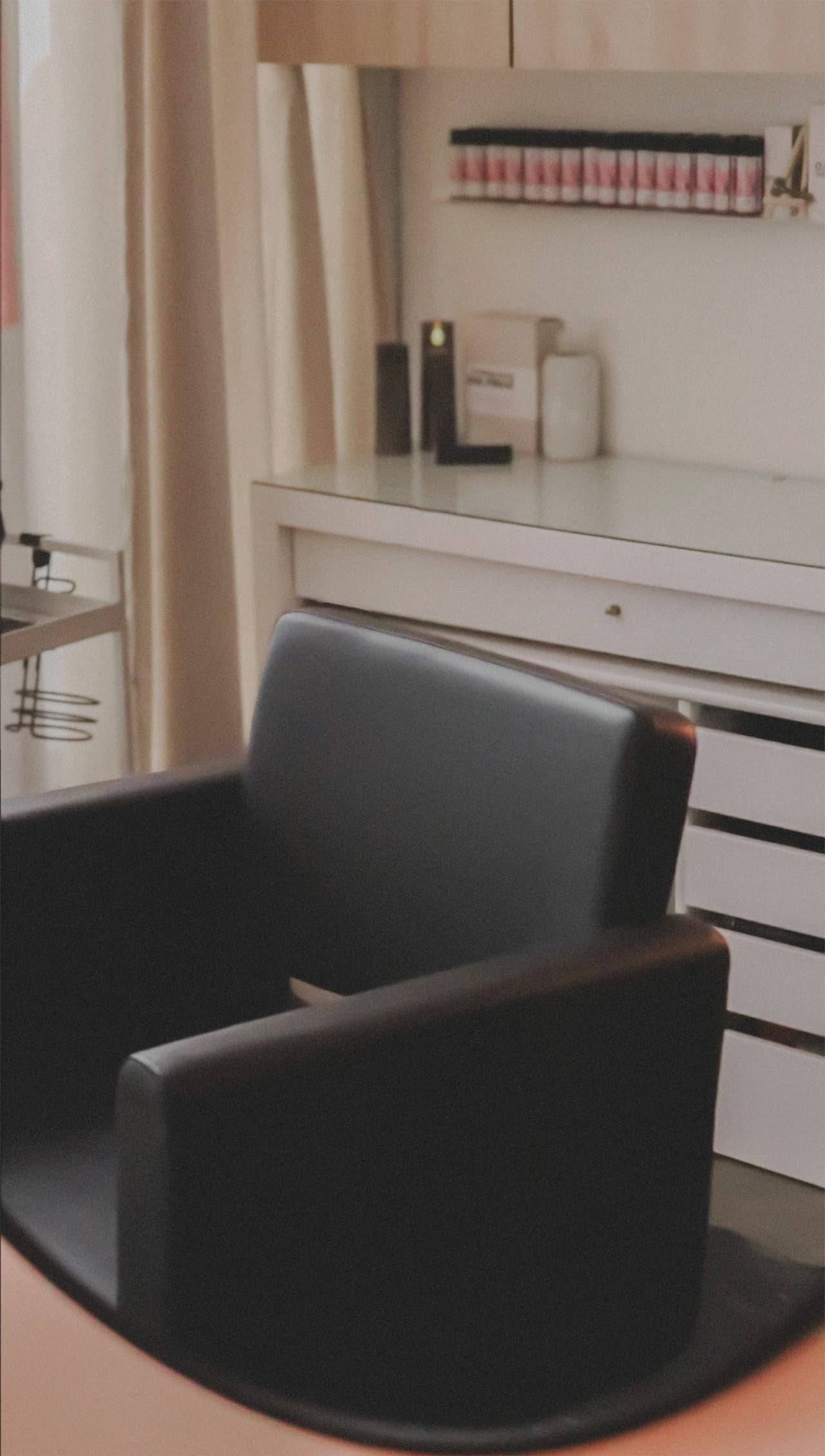 Close view of the black styling chair in The Sanctuary, in front of a white vanity and a row of colour tubes