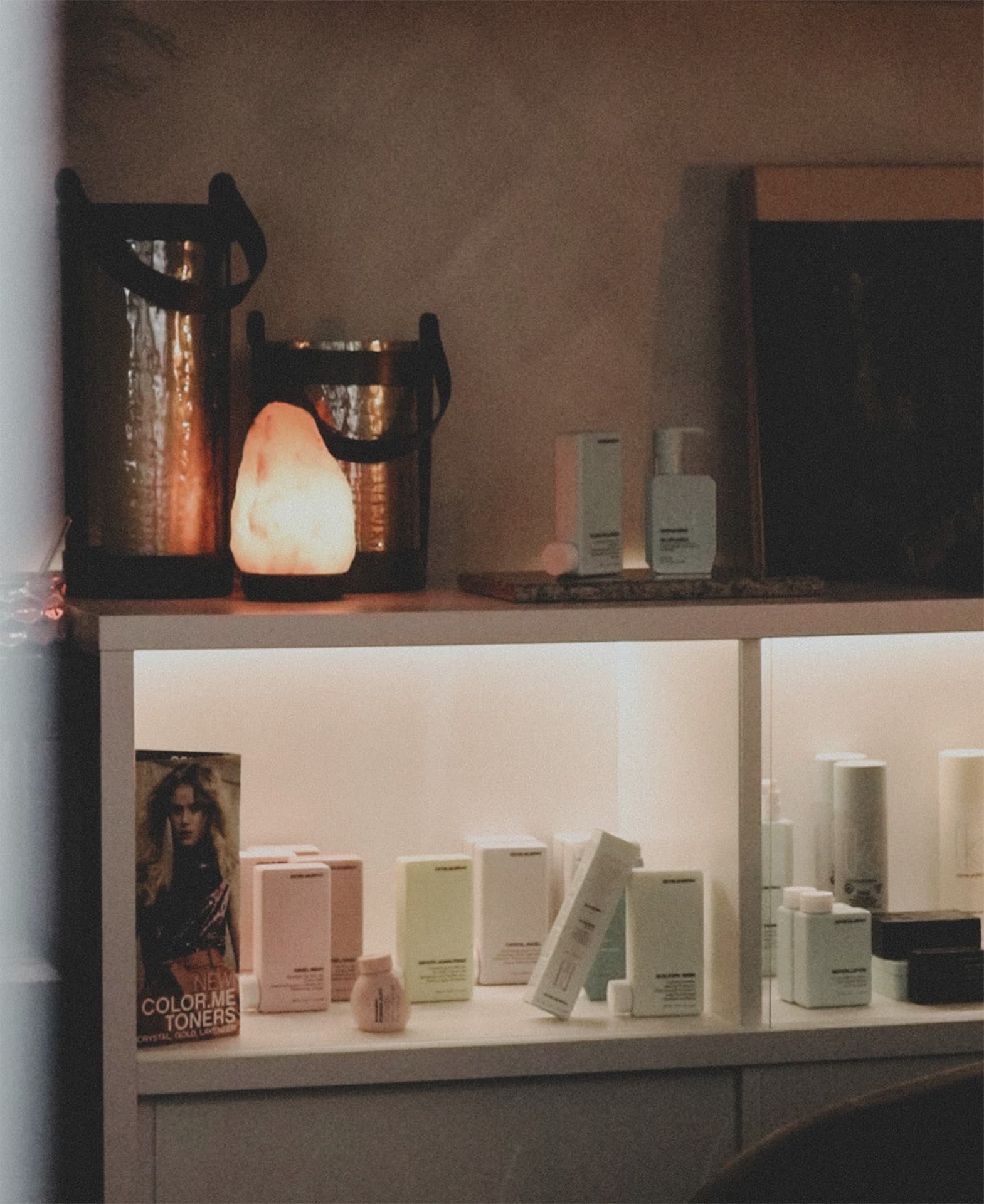 A shelf in The Sanctuary suite: a glowing salt lamp and lanterns above lit shelves of Kevin.Murphy hair care