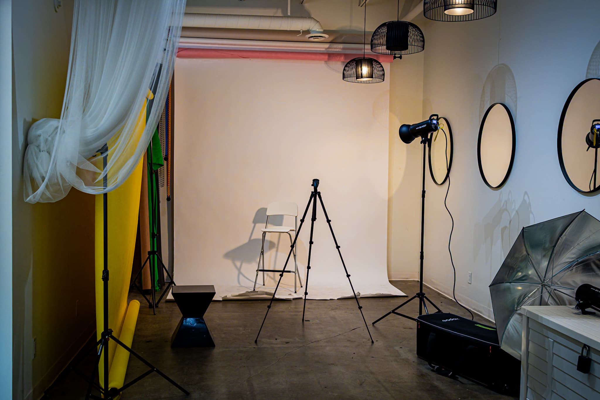 Photo studio with a tripod, studio lights, sheer drapes and round mirrors at House of Snob in Edmonton