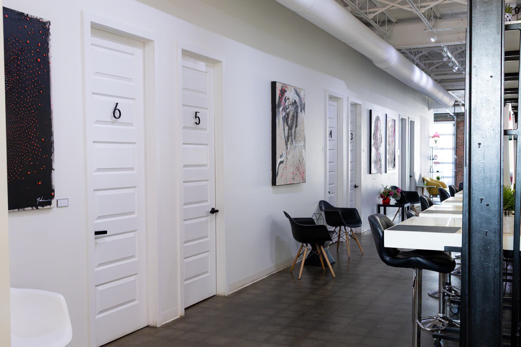 Corridor of numbered private suites with artwork and workstations at House of Snob in Edmonton
