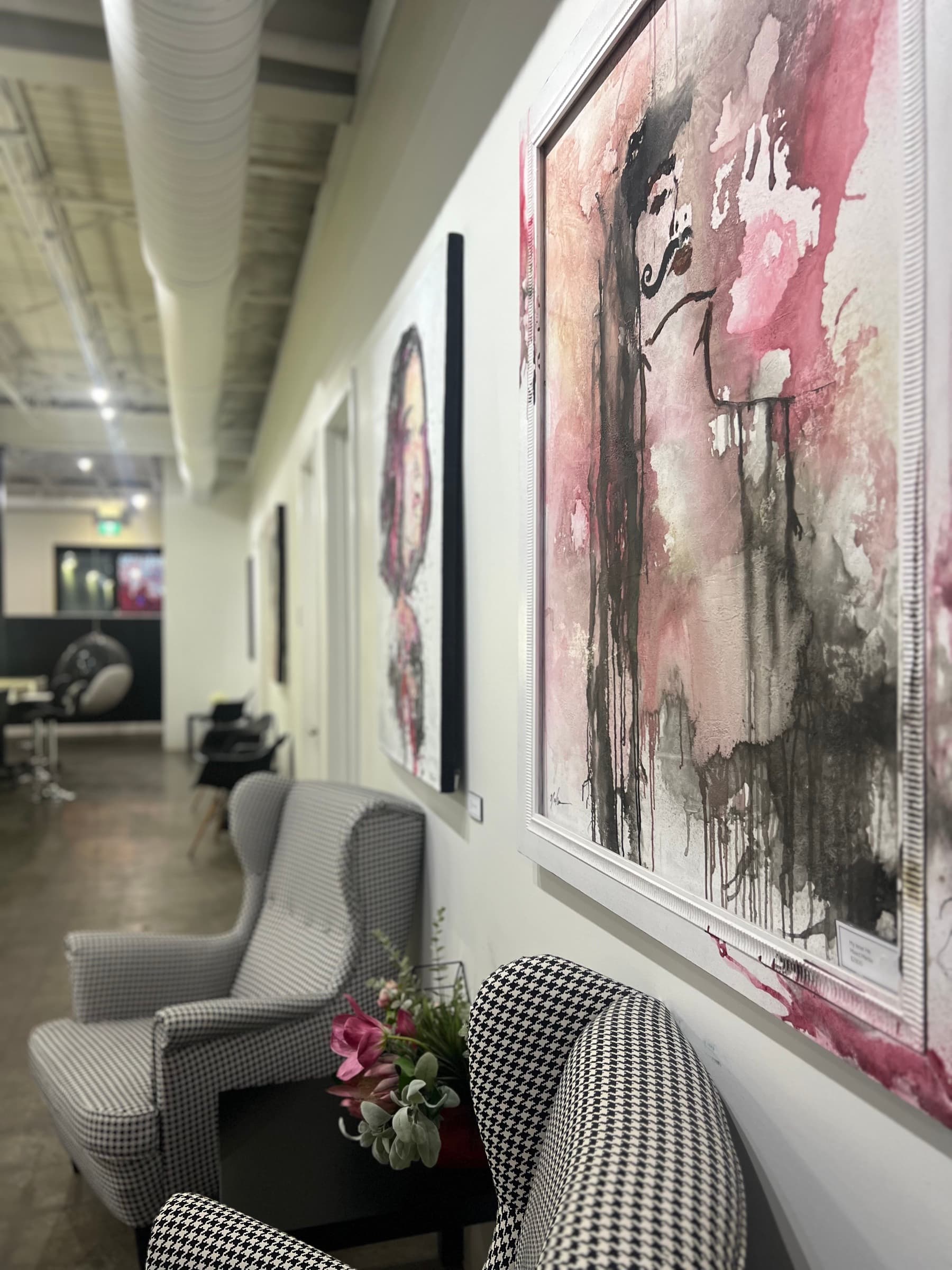 Wall of pink and black abstract art beside houndstooth armchairs at House of Snob in Edmonton