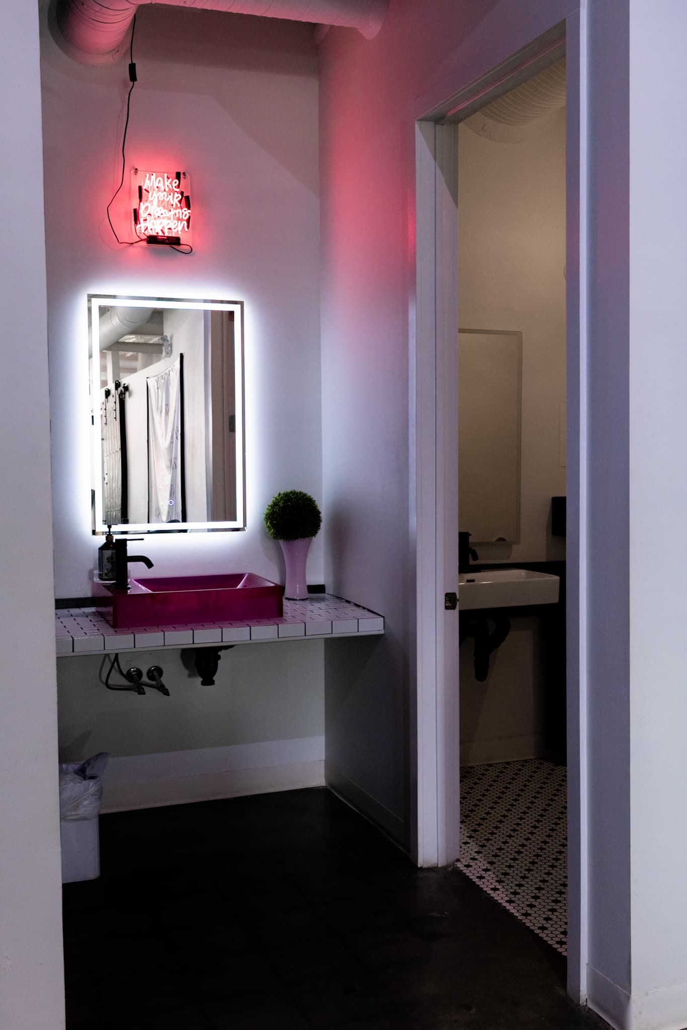 Pink sink vanity under a lit mirror and a pink neon sign at House of Snob in Edmonton
